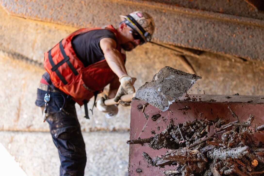 A crew member shovels debris aboard a working barge at a river lock.