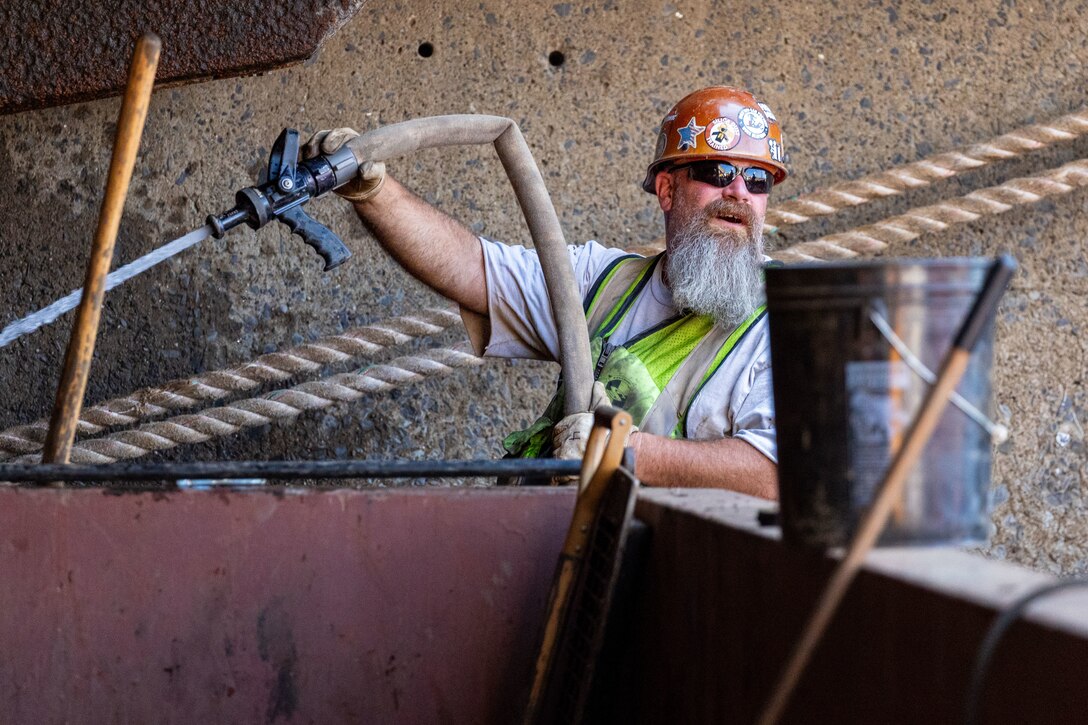 A crew member hoses off debris aboard a working barge at a river lock.