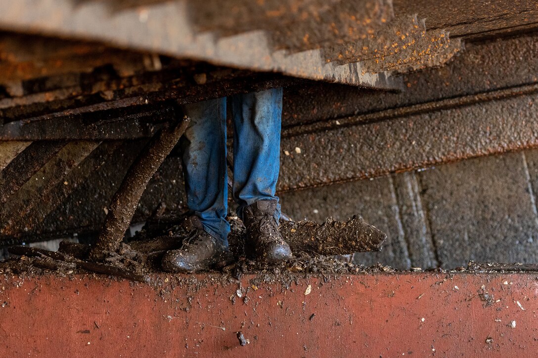 A maintenance worker descends from inside a dam gate on a working barge at a river lock.