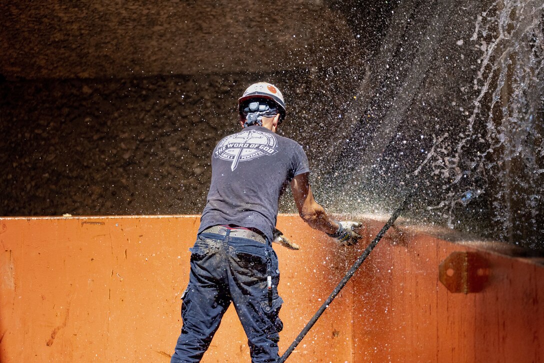 A maintenance worker cleans his gloves on a working barge at a river lock.