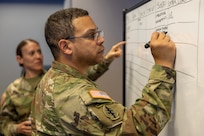 Master Sgt. Marcus Pirela, 45th Finance Center plans and operations advisor, marks a board as Maj. Sonja Keith, 45th FC Chief of Operations, makes remarks during a staff exercise at the Maj. Gen. Emmett J. Bean Federal Center in Indianapolis Oct. 28, 2024. The U.S. Army Financial Management Command hosted the exercise to increase its operational capabilities through the four phases of the conflict continuum, reduce its inefficiencies in battle tasks, and clearly identify financial management roles, responsibilities and authorities. (U.S. Army photo by Mark R. W. Orders-Woempner)
