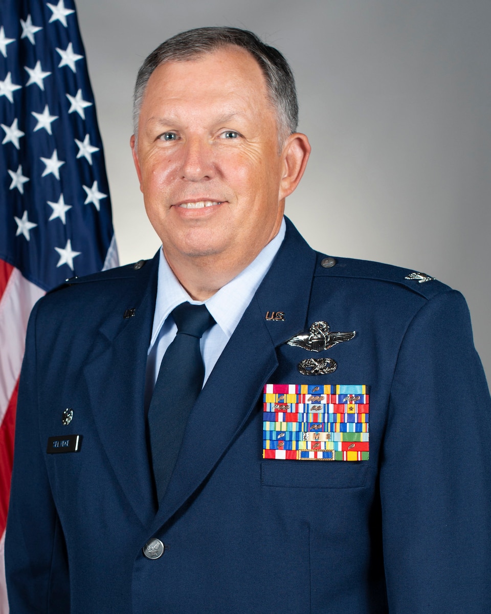 portrait of Col. Ron Selvidge in front of a U.S. flag and a grey background.