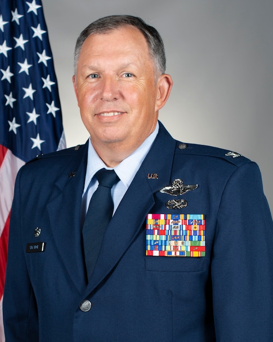 portrait of Col. Ron Selvidge in front of a U.S. flag and a grey background.
