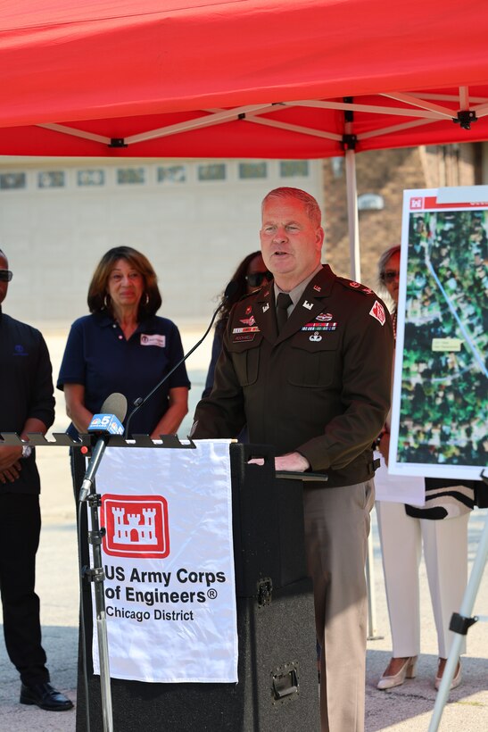 Army commander stands behind U.S. Army Corps of Engineers podium to give ceremony remarks with red canopy above.