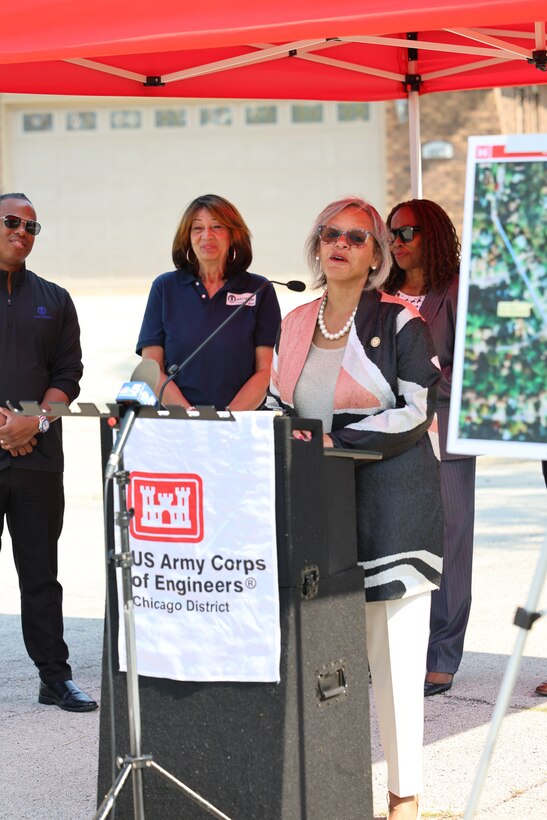 Woman stands behind U.S. Army Corps of Engineers podium to give comments during ceremony with red canopy above.