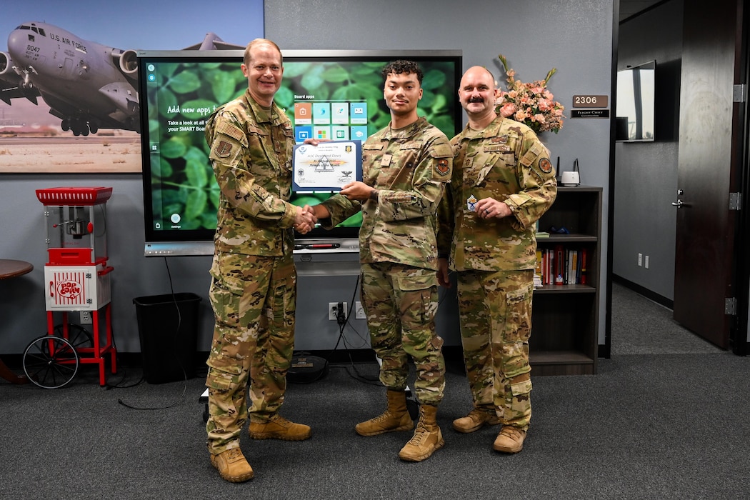 U.S. Air Force Col. Richard Kind, 97th Air Mobility Wing (AMW) commander, and Chief Master Sgt. Jonny Adams, 97th AMW command chief, hands an award to Airman 1st Class Desmond Davis, 97th Contracting Flight contracting specialist, at Altus Air Force Base, Oklahoma, Aug 1, 2025. Davis was awarded Airman of the Month for June, a title given to outstanding Airmen. (U.S. Air Force photo by Airman 1st Class Lauren Torres)