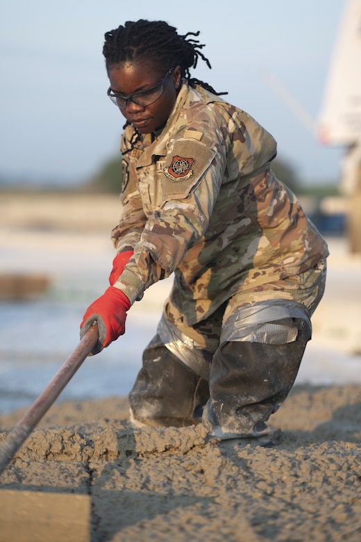 Airman 1st Class Deborah Wembabazi, a heavy equipment specialist with the 157th Civil Engineer Squadron, levels concrete during a prime base engineer emergency force training at the 201st Regional Training Site, Fort Indiantown Gap, Pennsylvania, July 30, 2025. The engineers poured concrete and constructed an expeditionary runway while honing Prime BEEF processes and skill sets. (U.S. Air National Guard photo by Tech. Sgt. Victoria Nelson)