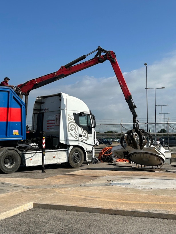 A truck with a grabber grabs a chunk of metal.