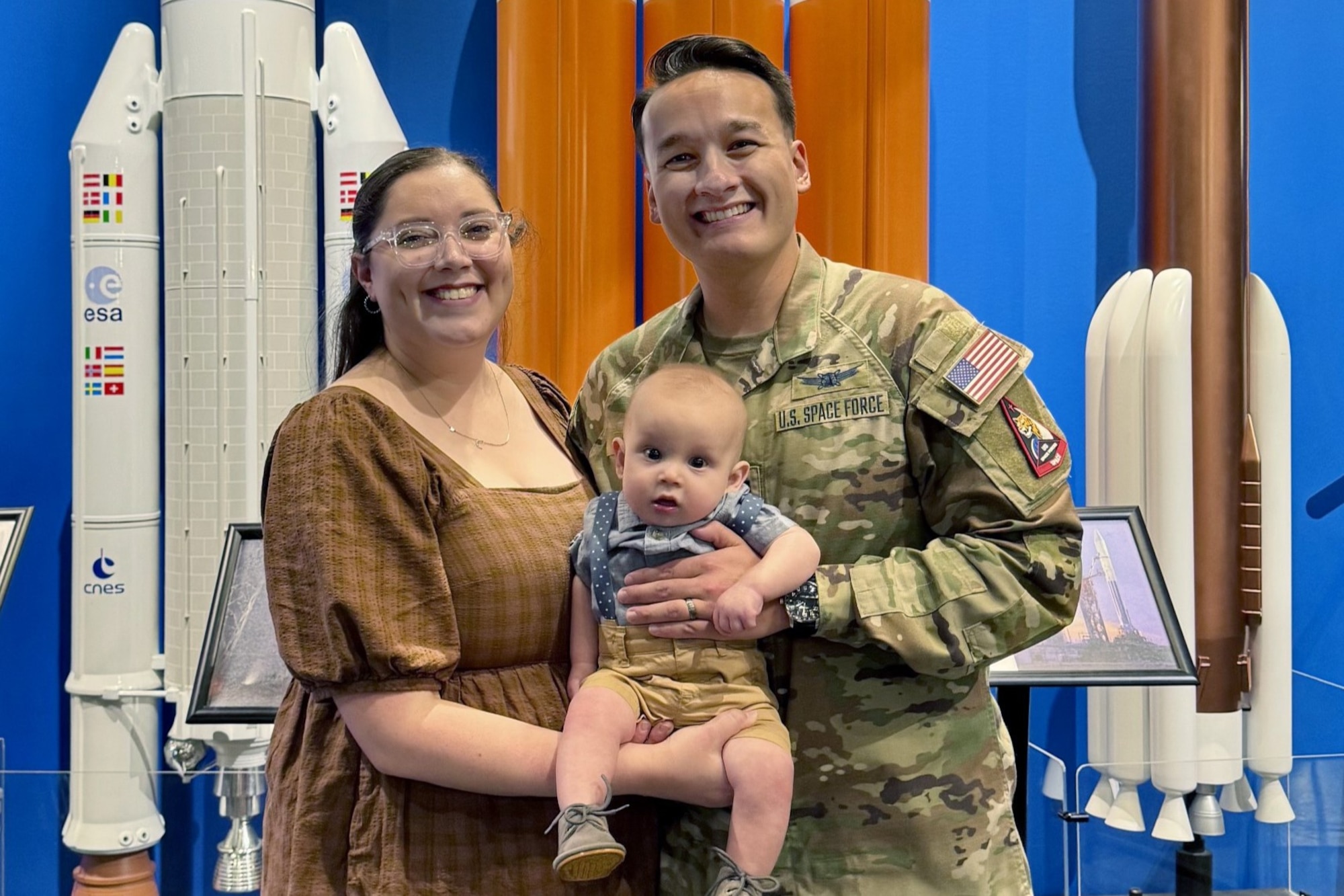 A family of three smile for the camera in front of rocket booster displays.