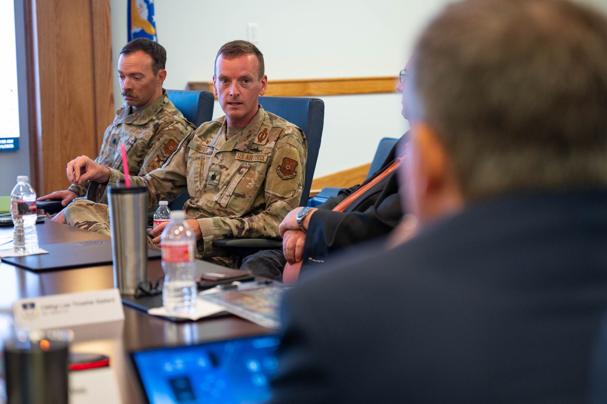 A man in uniform talks across a table to a man in civilian attire.