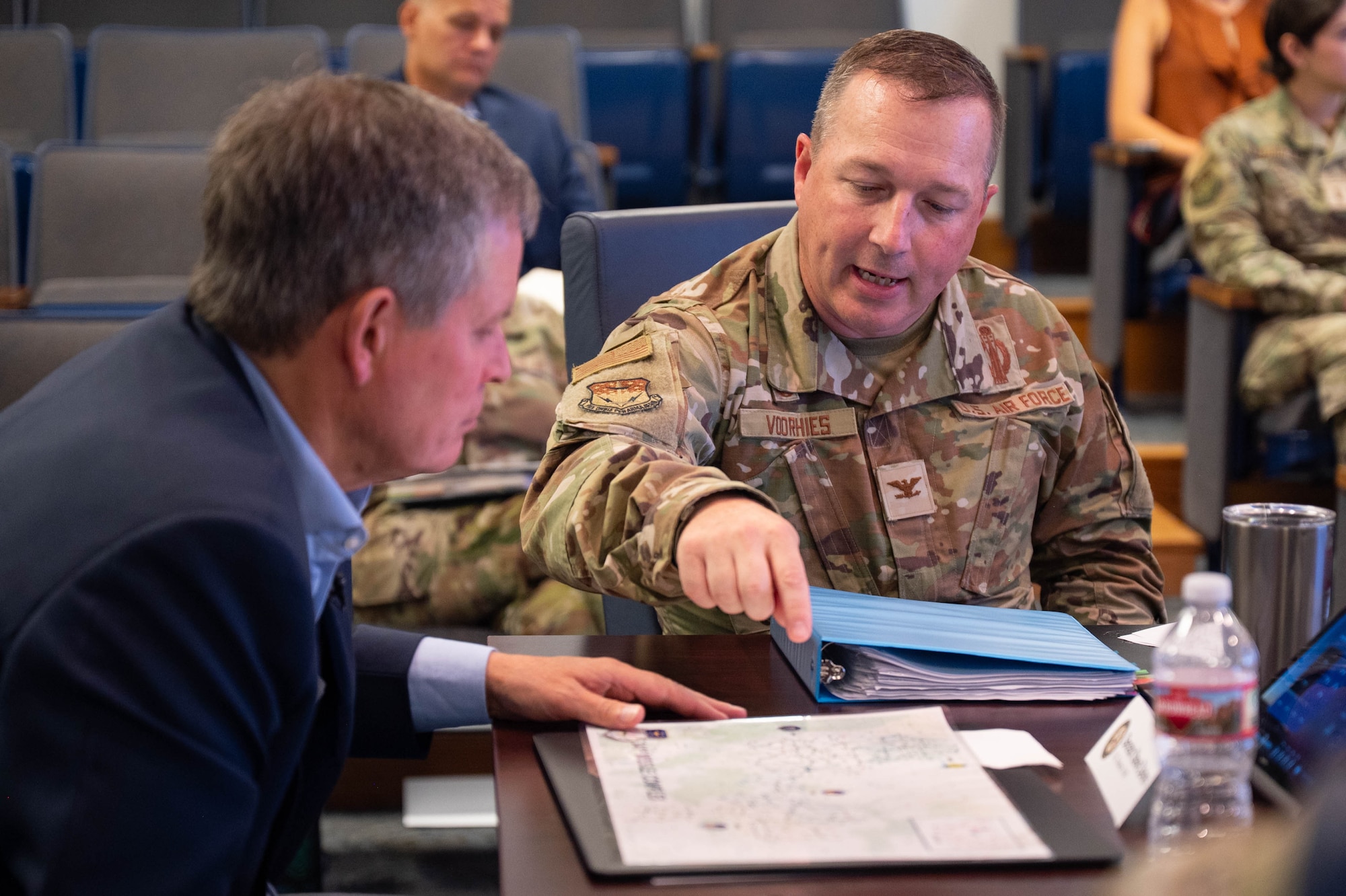 A man in uniform explains a map to a man in civilian attire.