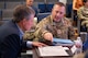 A man in uniform explains a map to a man in civilian attire.
