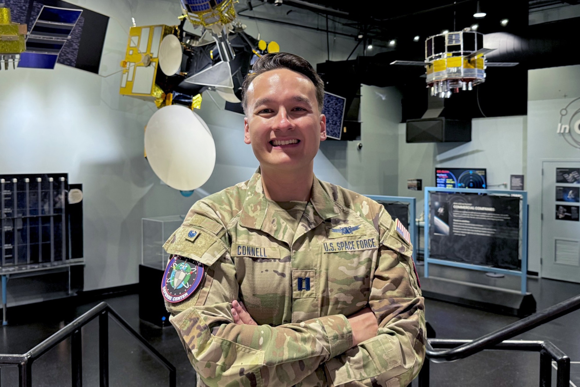 A man in military uniform stands with his arms crossed smiling into the camera.