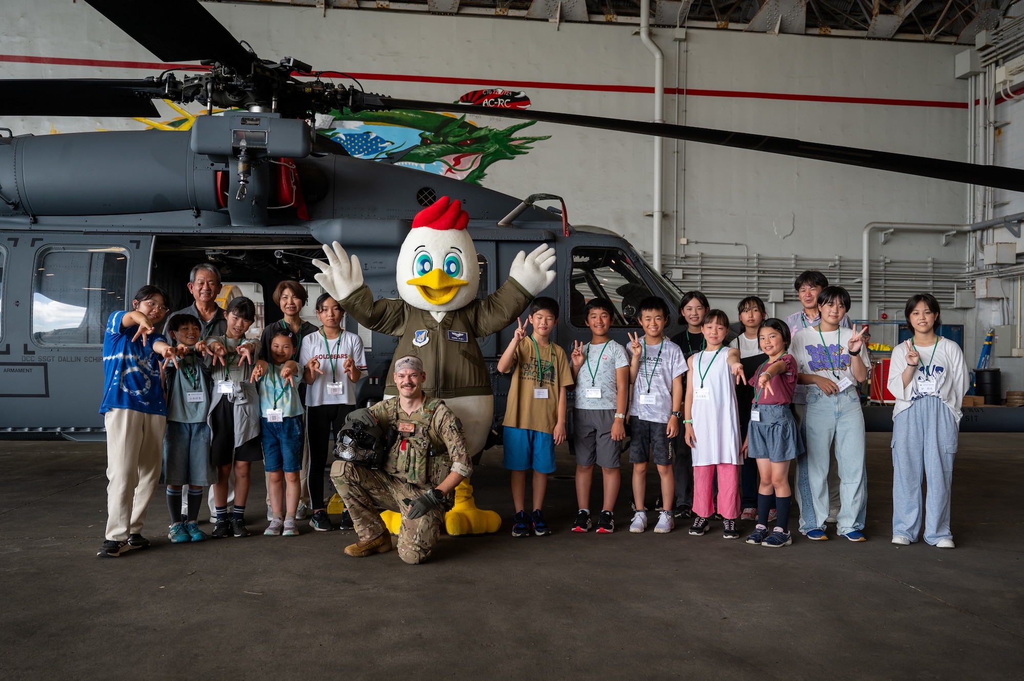 Achi-mura students and Kadena Airmen pose for a photo in front of an HH-60