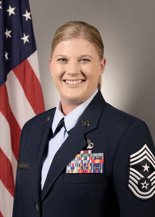 A woman wearing Air Force service dress with an American flag draped in the background.