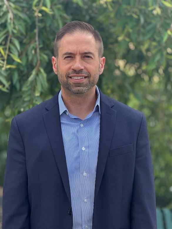 A man in a suit poses for a photo outside.