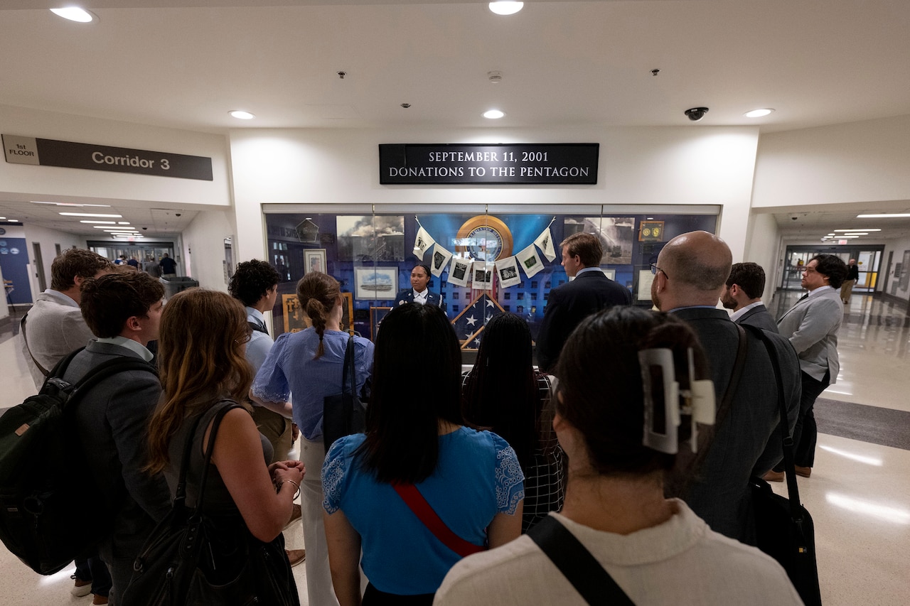 More than a dozen people gather around a tour guide by an exhibit inside the Pentagon.