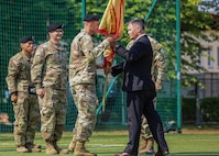 U.S. Army Col. Jeremy McHugh, incoming commander of U.S. Army Garrison Poland, left, takes part in the traditional “passing of the guidon” by receiving the USAG-Poland guidon from Tommy Mize, right, Director of Installation Management Command Europe, during the Garrison’s change of command ceremony, Camp Kościuszko, Poland, July 15, 2025. Established on March 21, 2023, USAG Poland supports 7,500 American Soldiers across 12 sites, delivering quality infrastructure and services to enable V Corps readiness and stands as the Army’s home on the Eastern Flank. (U.S. Army photo by Sgt. Devin Klecan)