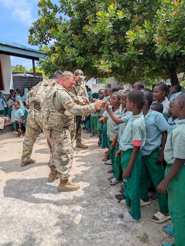 Men in military uniforms engage with Kenyan children in school uniforms with dark green pants and light green shirts.