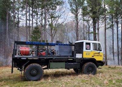 a large truck with a flat bed and some equipment sitting on the flat bed sits in a wooded aera with smoke in the trees.