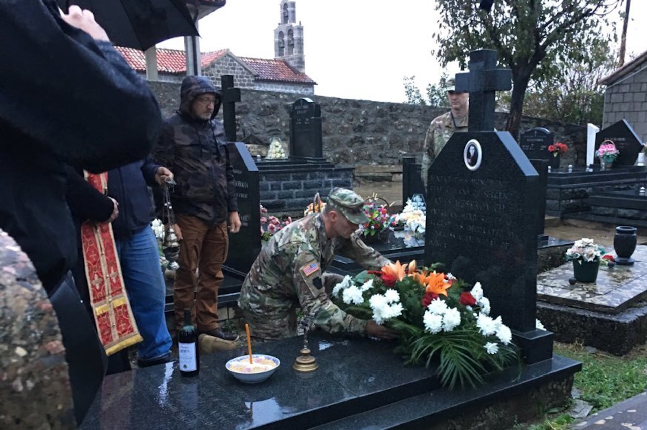 A soldier places a wreath on top of a large gravestone in a cemetery.