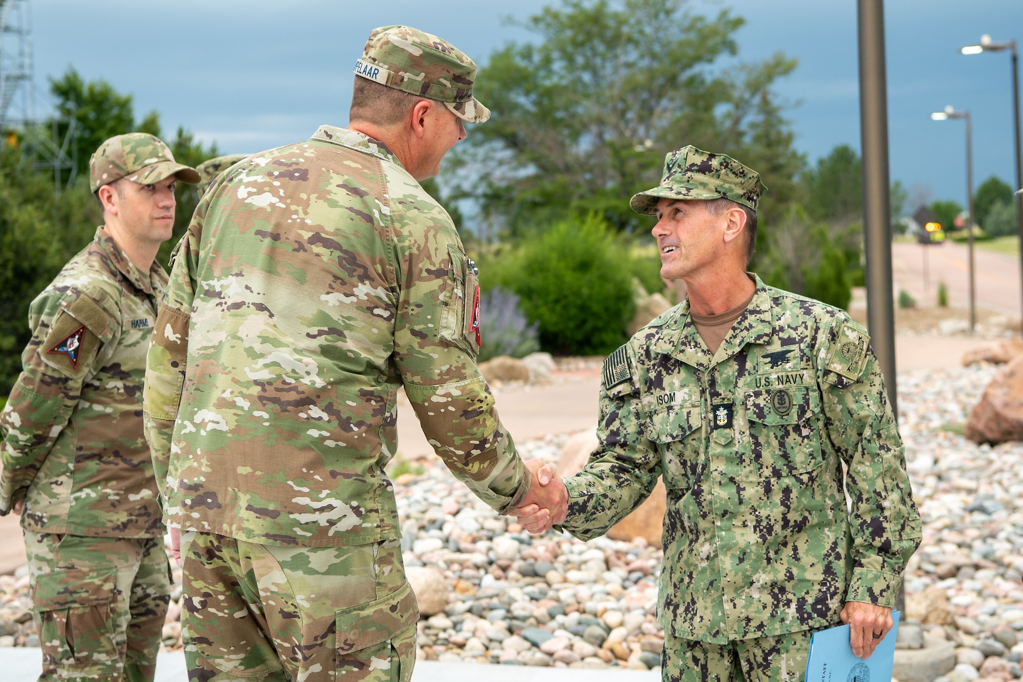 Military members in uniform shake hands with each other outside.