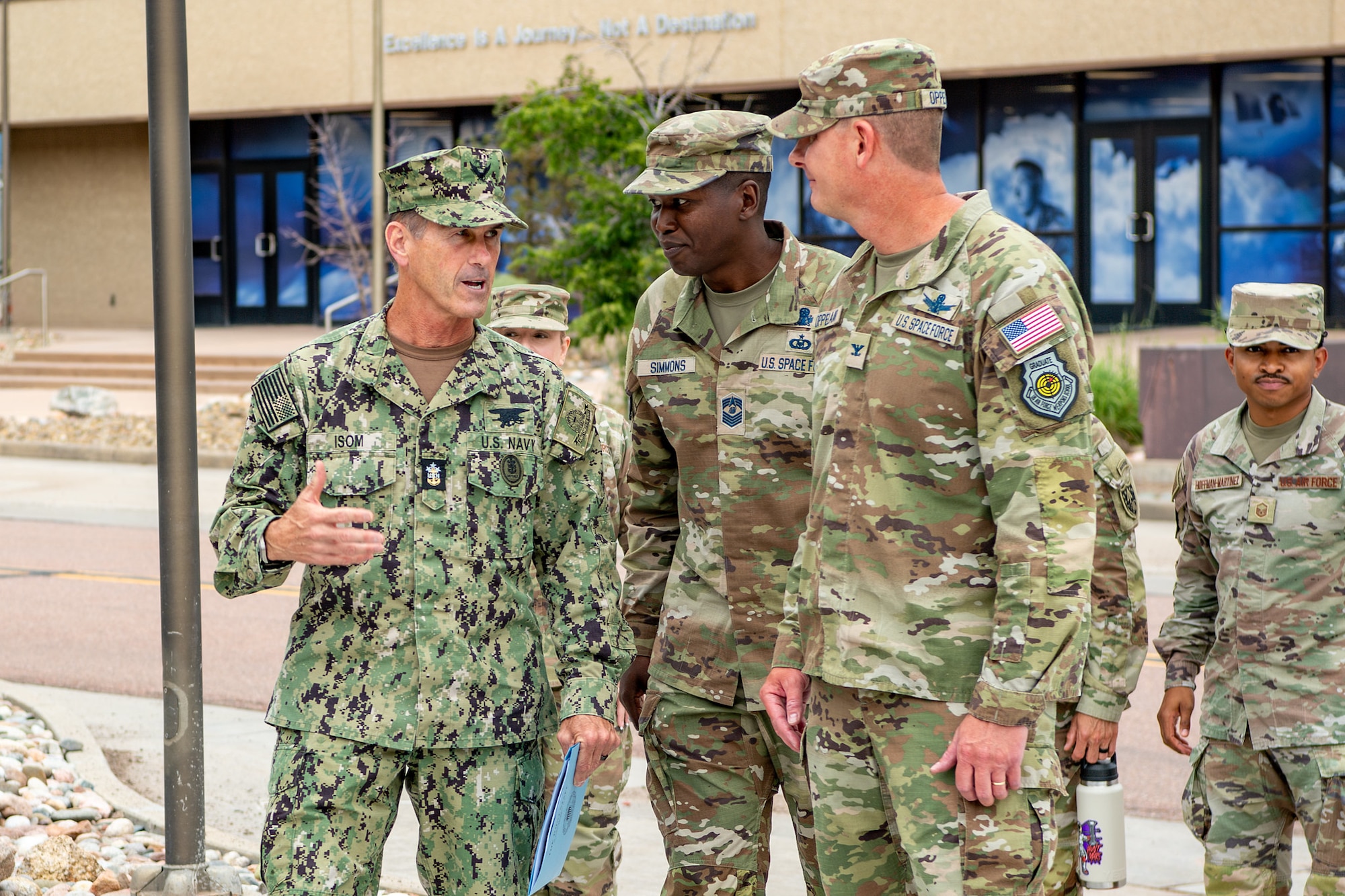 Military members in uniform talk with one another outside.