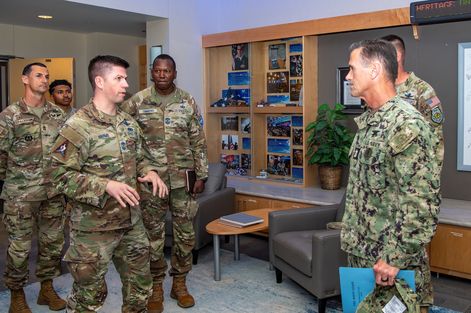 Military members in uniform talk with one another in a room.