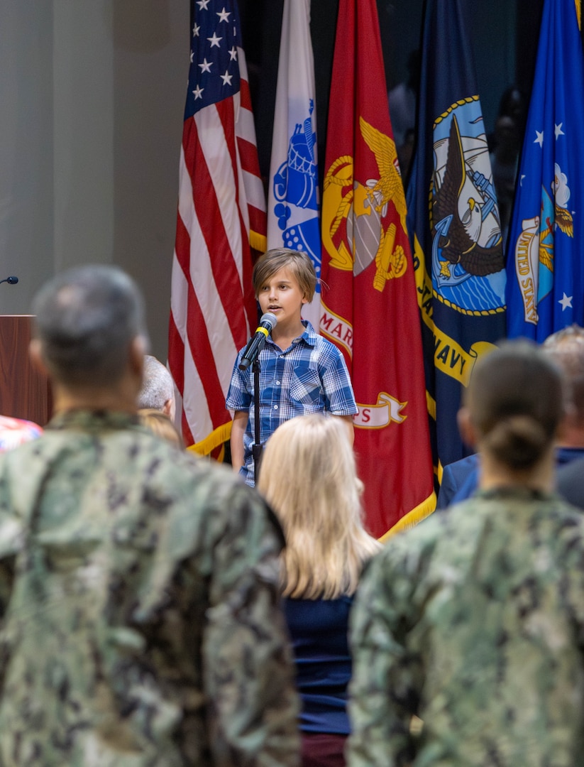 A boy sings the National Anthem in an auditorium.