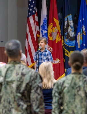 A boy sings the National Anthem in an auditorium.