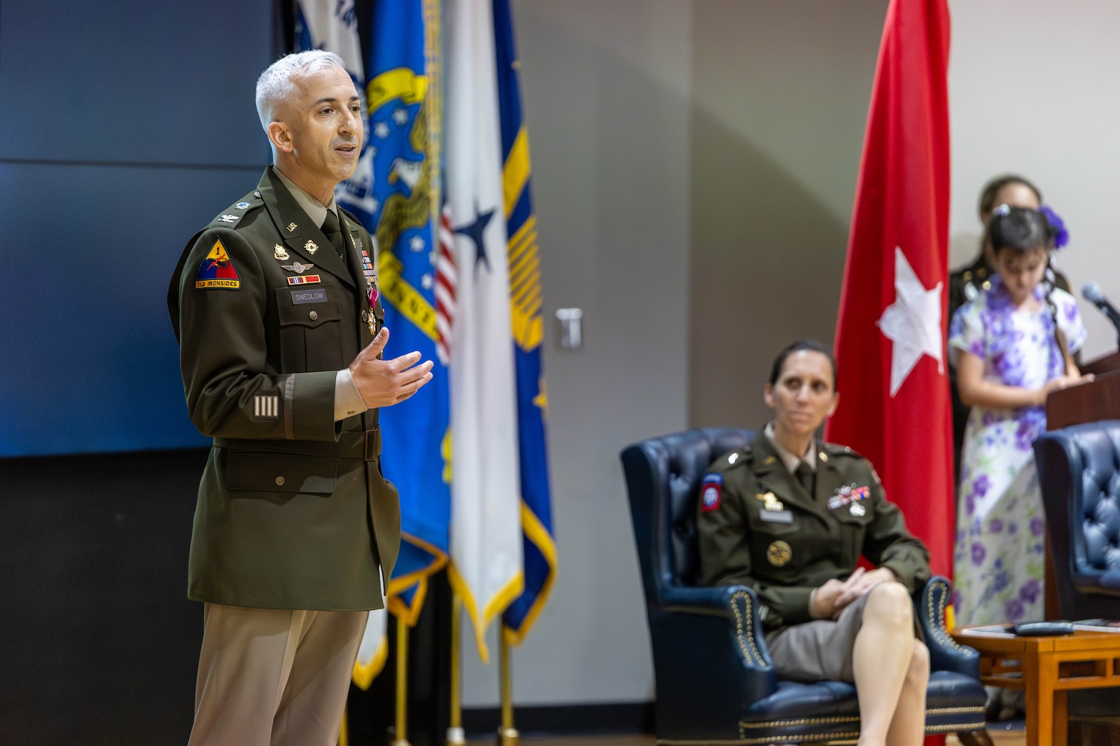 A man in uniform speaks on a stage in an auditorium.