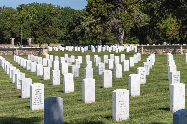 White headstones are lined up in green grass with trees in the background.