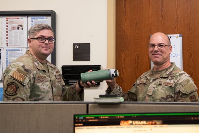 Two Airmen hold either end of a water bottle and smile at the camera.