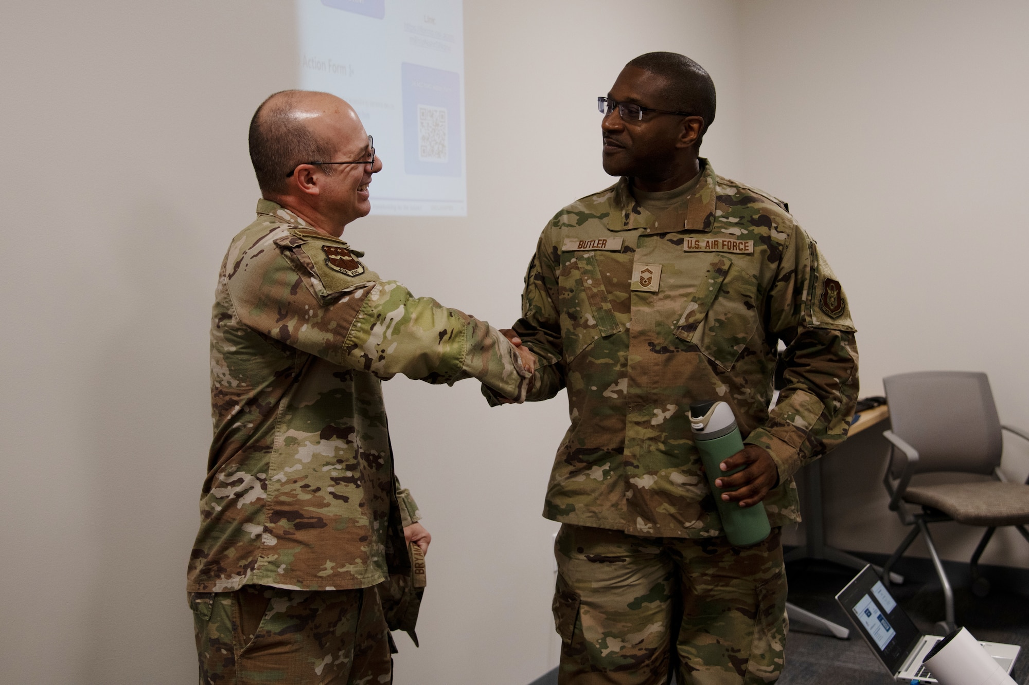 Two airmen shake hands, and one holds a water bottle.