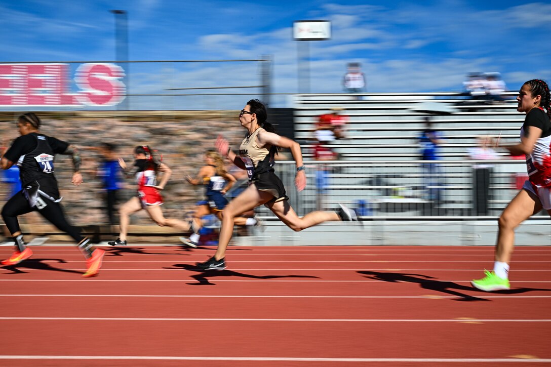 A female athlete runs on a track during the day surrounded by other runners.