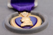 A closeup of a gold medal with George Washington's profile and a purple ribbon is shown.