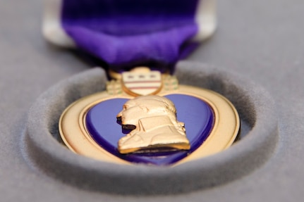 A closeup of a gold medal with George Washington's profile and a purple ribbon is shown.