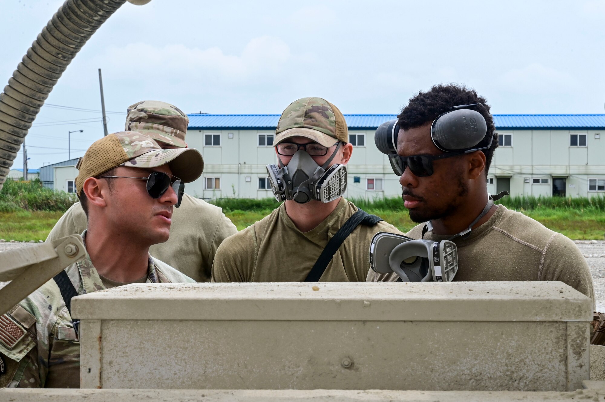 U.S. Air Force Staff Sgt. Uriel Ortiz (left), 8th Civil Engineer Squadron (CES) pavements and equipment Airman, U.S. Air Force Senior Airman Colton Behrends (middle), 8th CES pavements and equipment operator, and U.S. Air Force Senior Airman Ricky Steed, 8th CES pavements and equipment journeyman, discuss how to use controls on a concrete mixing truck during exercise Beverly Sentinel 25-3 at Kunsan Air Base, Republic of Korea, Aug. 6, 2025. The 8th CES prepared a cement truck to patch damaged areas on a simulated flightline area.