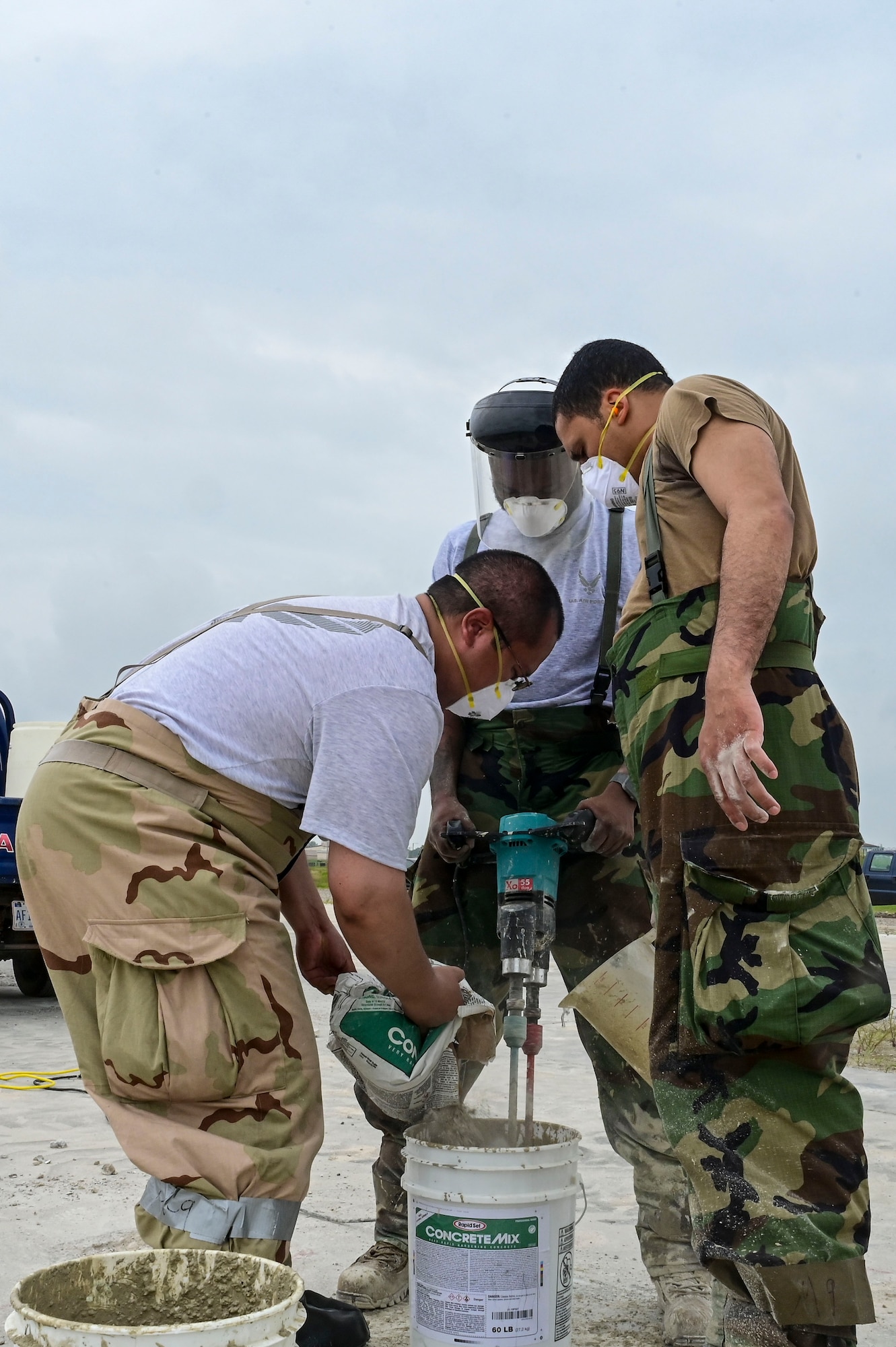 U.S. Air Force Staff Sgt. Luis Romano (left), 8th Civil Engineer Squadron heating, ventilation and air conditioning  spall team member, U.S. Air Force Senior Airman Nasir Harding (middle), 8th CES HVAC spall team member, and U.S. Air Force Senior Airman Gabriel Vivas (right), 8th CES HVAC spall team member, mix quick concrete together to patch holes during exercise Beverly Sentinel 25-3 at Kunsan Air Base, Republic of Korea, Aug. 6, 2025. To practice Rapid Airfield Damage Repair (RA/DR), the Red Devils practiced patching holes on the flightline where they were required to cut out and level damaged spots, clean up concrete debris, mix and pour concrete.