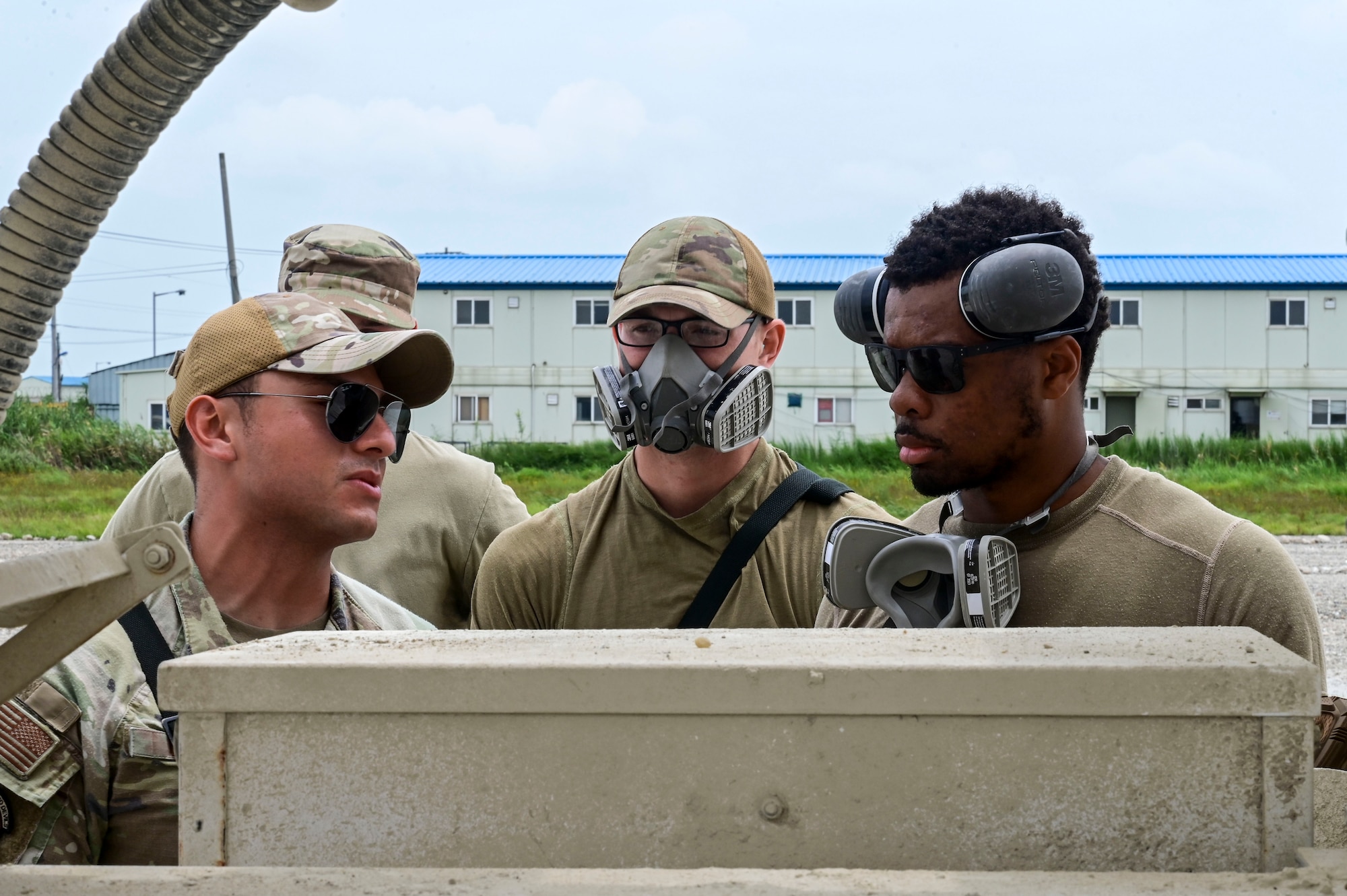 U.S. Air Force Staff Sgt. Uriel Ortiz (left), 8th Civil Engineer Squadron (CES) pavements and equipment Airman, U.S. Air Force Senior Airman Colton Behrends (middle), 8th CES pavements and equipment operator, and U.S. Air Force Senior Airman Ricky Steed, 8th CES pavements and equipment journeyman, discuss how to use controls on a concrete mixing truck during exercise Beverly Sentinel 25-3 at Kunsan Air Base, Republic of Korea, Aug. 6, 2025. The 8th CES prepared a cement truck to patch damaged areas on a simulated flightline area.