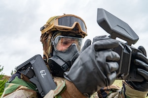 An airman in a gas mask uses a controller to fly a drone