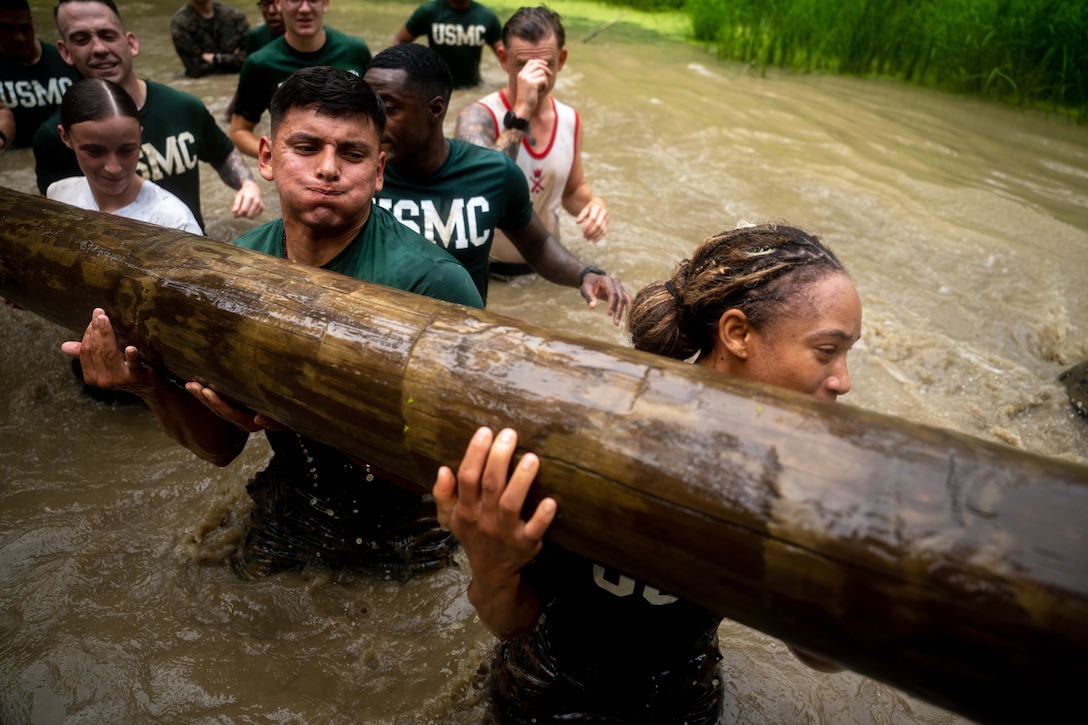 Marines carry a log while walking through murky waters.