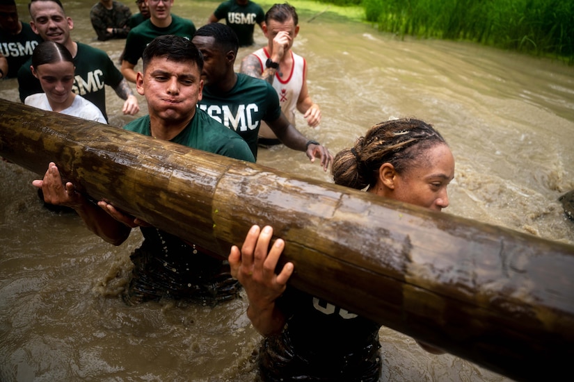 Marines carry a log while walking through murky waters.