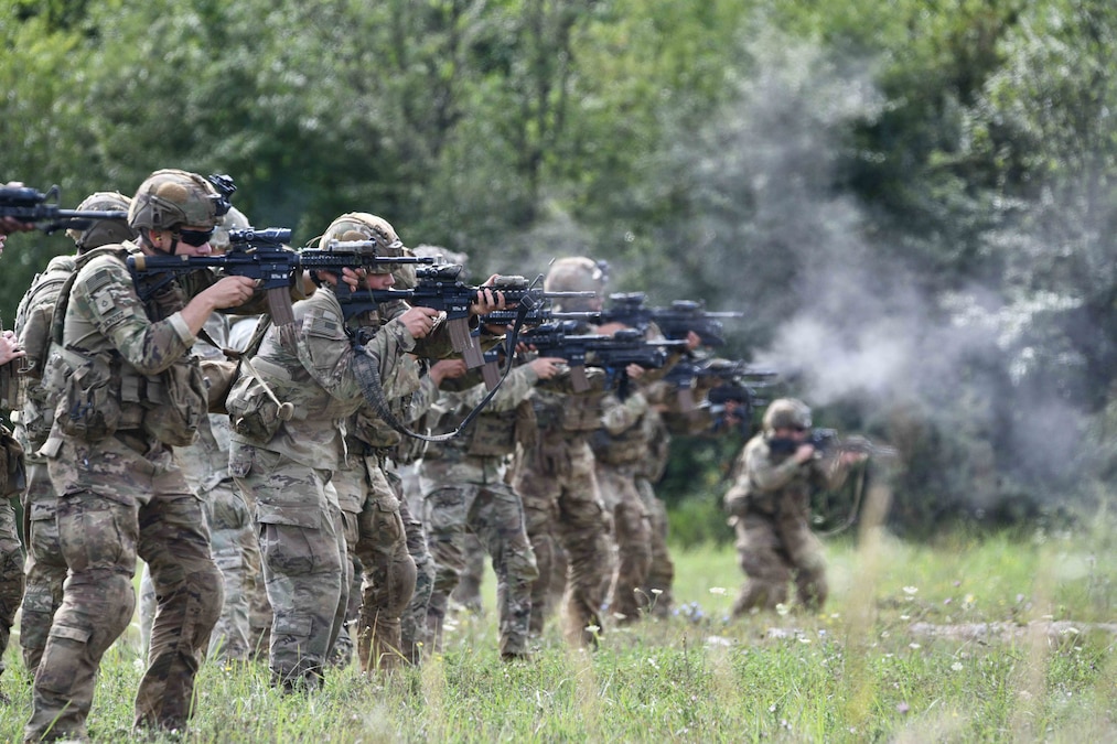 Soldiers standing in formation fire weapons in a field.