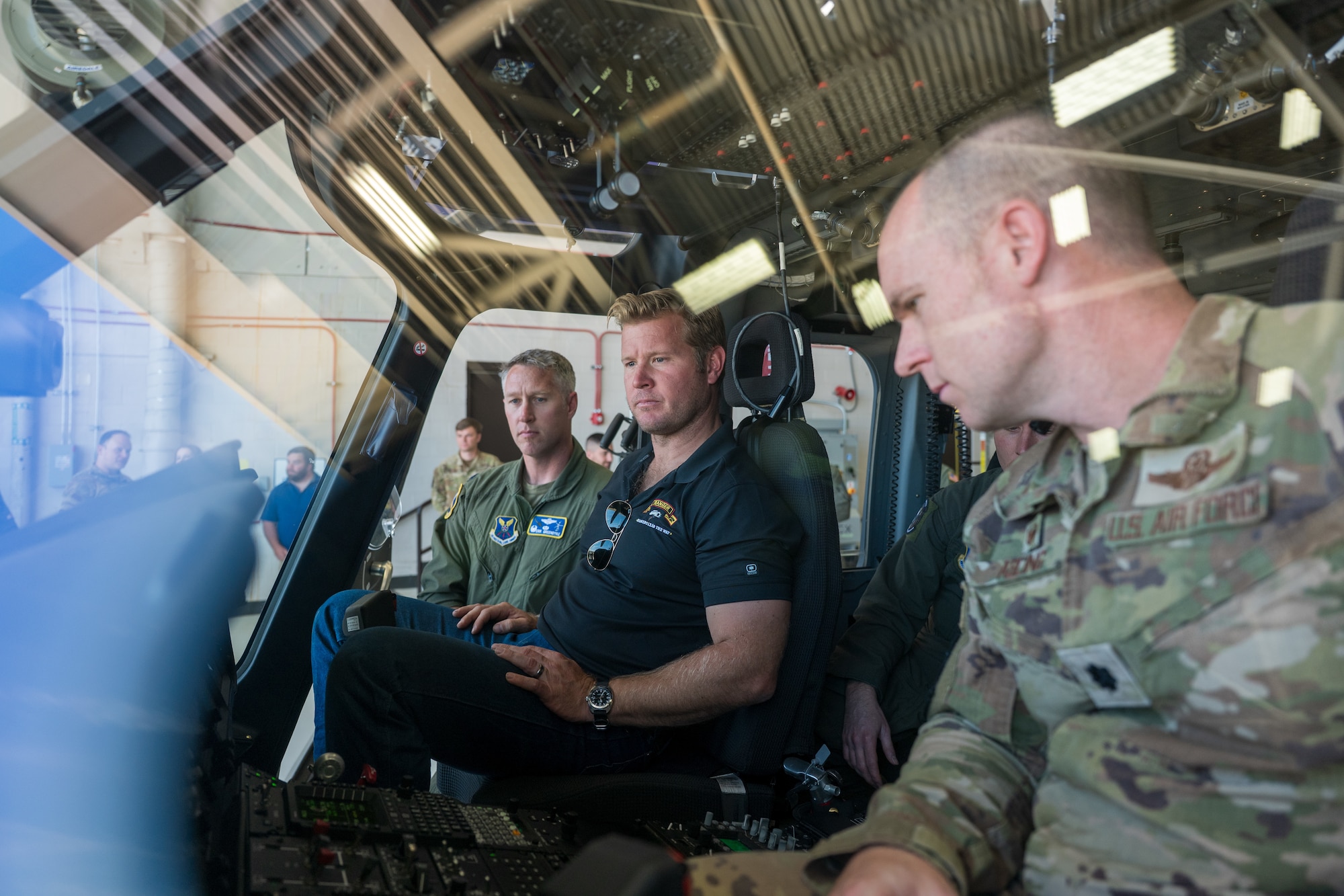 A man in civilian attire sits next to a man in uniform on a helicopter.