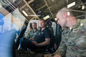 A man in civilian attire sits next to a man in uniform on a helicopter.
