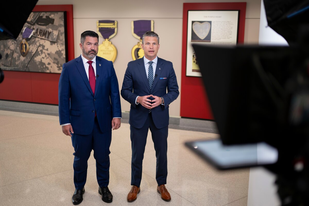 Two men stand next to each other in front of partially visible cameras and lights.