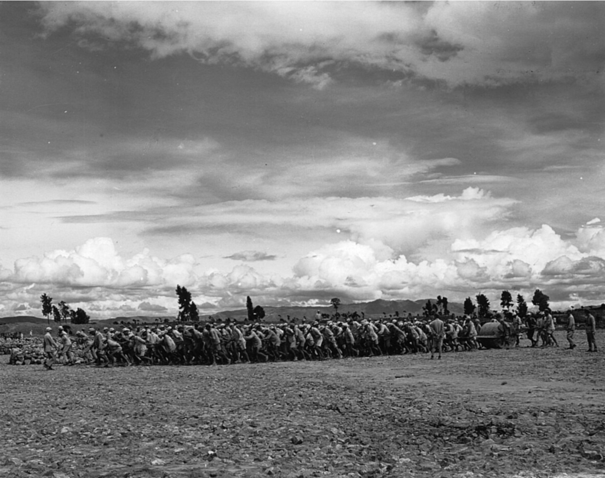 Hundreds of Chinese laborers pull a roller to smooth a runway for an airstrip.