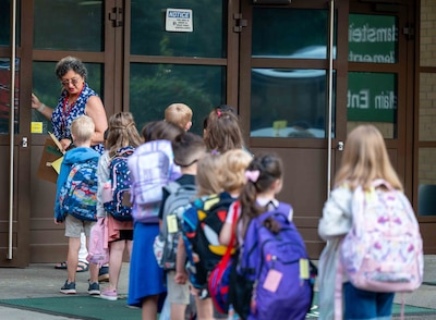 Female teacher leads a group of young students into school