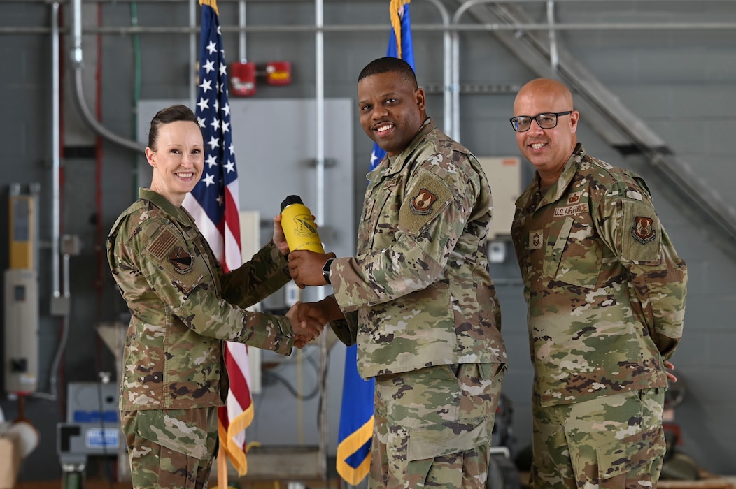 Three individuals wearing camouflage uniforms smile for a photo. The person in the middle is accepting an award—a yellow water bottle engraved with the 88th Mission Support Group patch.